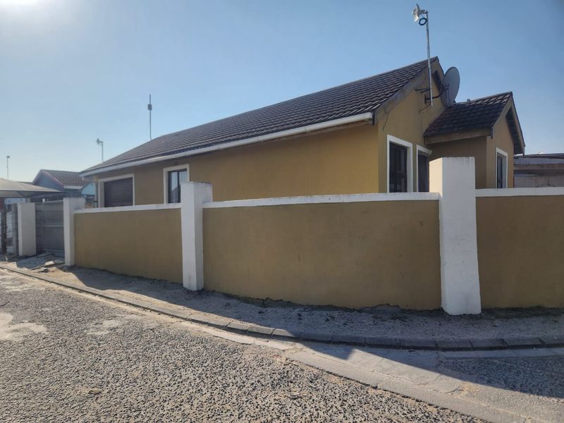 Street view of a single-story house featuring a tiled roof and a solid perimeter wall with white pillars.