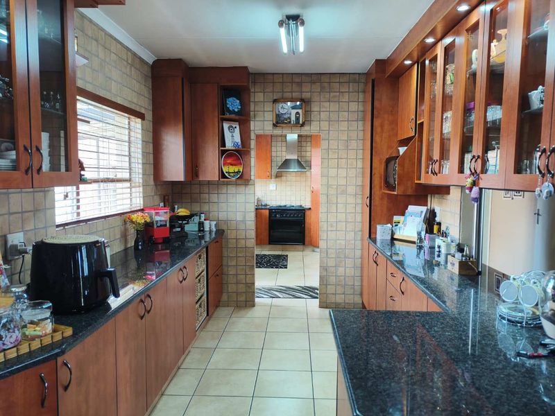 A functional kitchen featuring extensive wooden cabinetry, granite countertops, tiled backsplash, and a separate scullery area with a built-in oven and extractor fan.