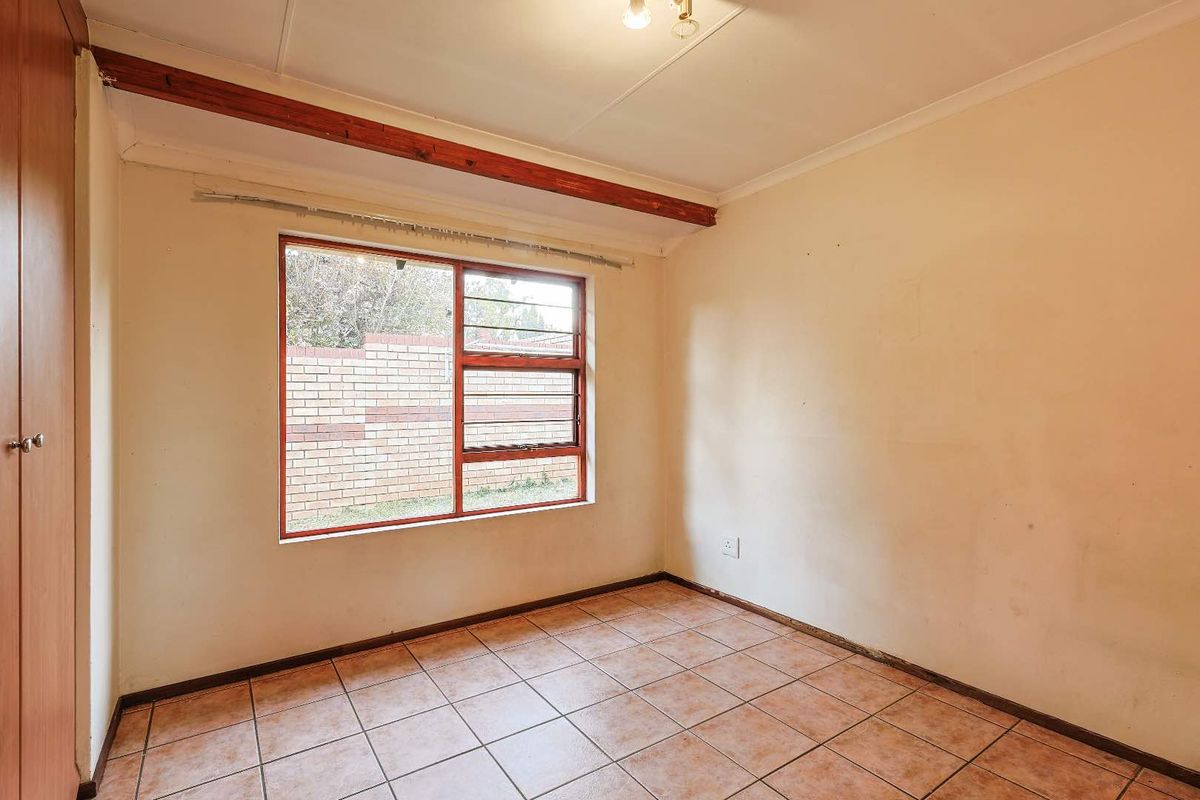 An empty bedroom featuring tiled flooring, a built-in wardrobe, and an exposed timber ceiling beam, offering a blank canvas for renovation.