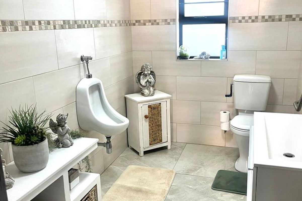 A modern bathroom featuring neutral wall tiles, a wall-mounted urinal, a standard toilet, and a vanity unit with a window for natural light.