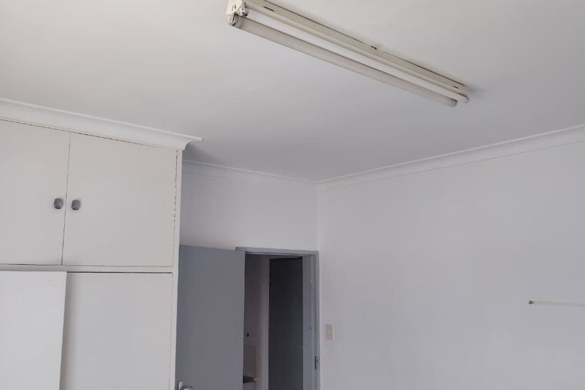 An empty bedroom featuring built-in cupboards, neutral walls, and a fluorescent ceiling light fixture.