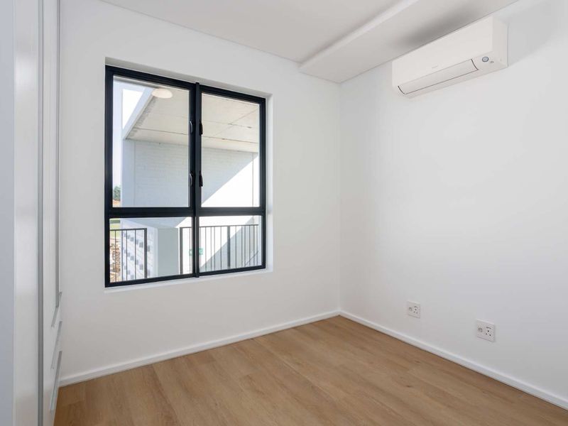 A bright, modern bedroom featuring laminate flooring, a built-in wardrobe, and a wall-mounted split-system air conditioner.