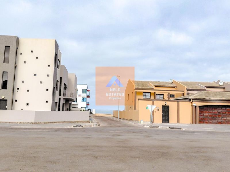 A street-level view of a residential area featuring modern townhouses and paved access roads leading toward the coast.
