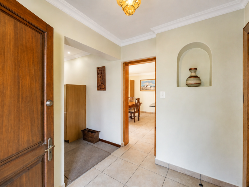 A bright entrance hallway featuring tiled flooring, a decorative arched wall niche, and classic wooden door frames leading into the home.