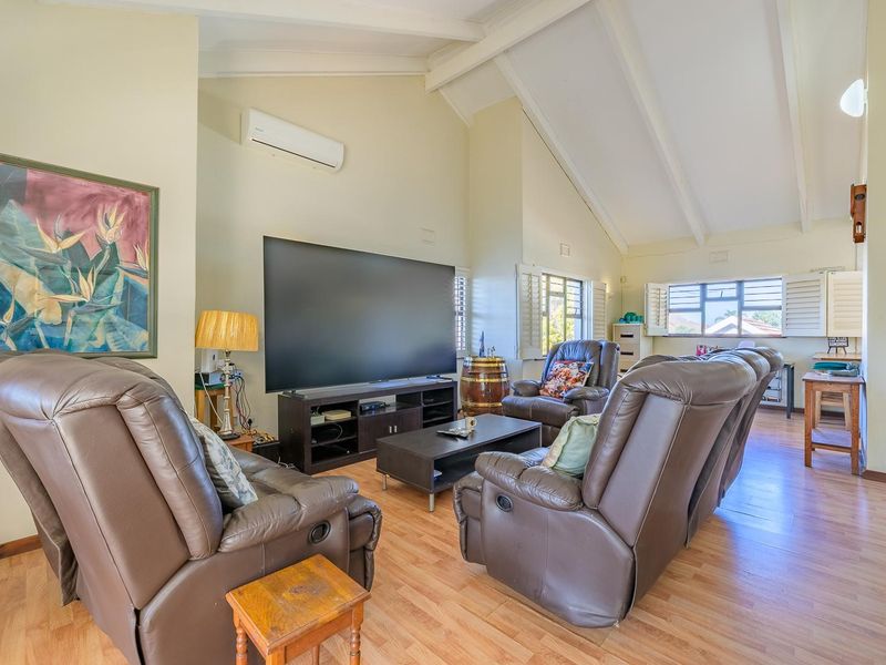 Spacious living room featuring high vaulted ceilings, laminate flooring, plantation shutters, and a wall-mounted split-system air conditioner.