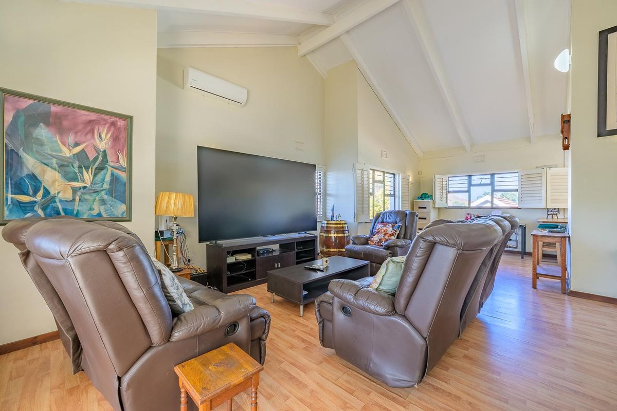 Spacious living room featuring high vaulted ceilings, laminate flooring, plantation shutters, and a wall-mounted split-system air conditioner.