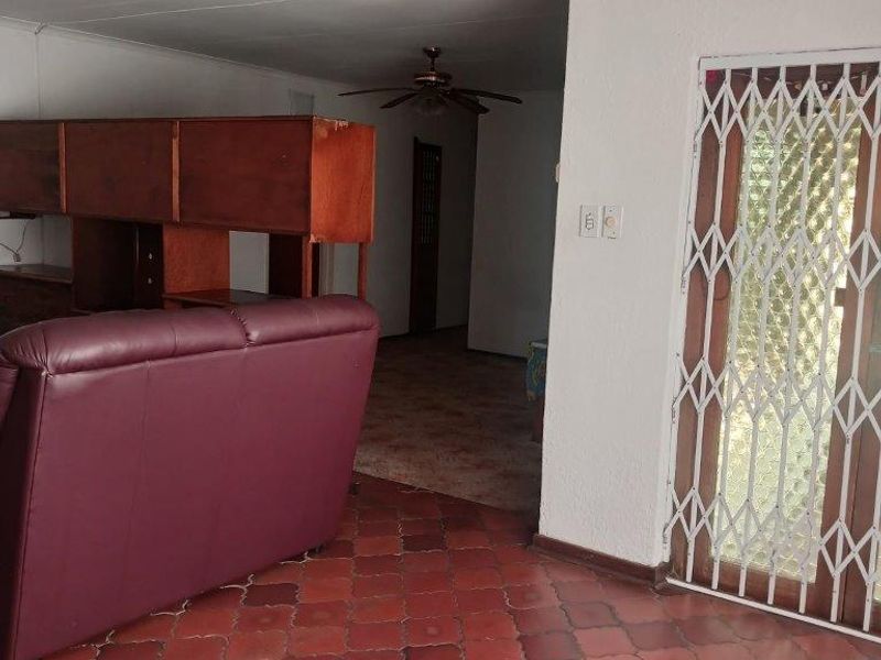 Living area featuring terracotta-style tiled flooring, a ceiling fan, and a secure metal entrance gate.