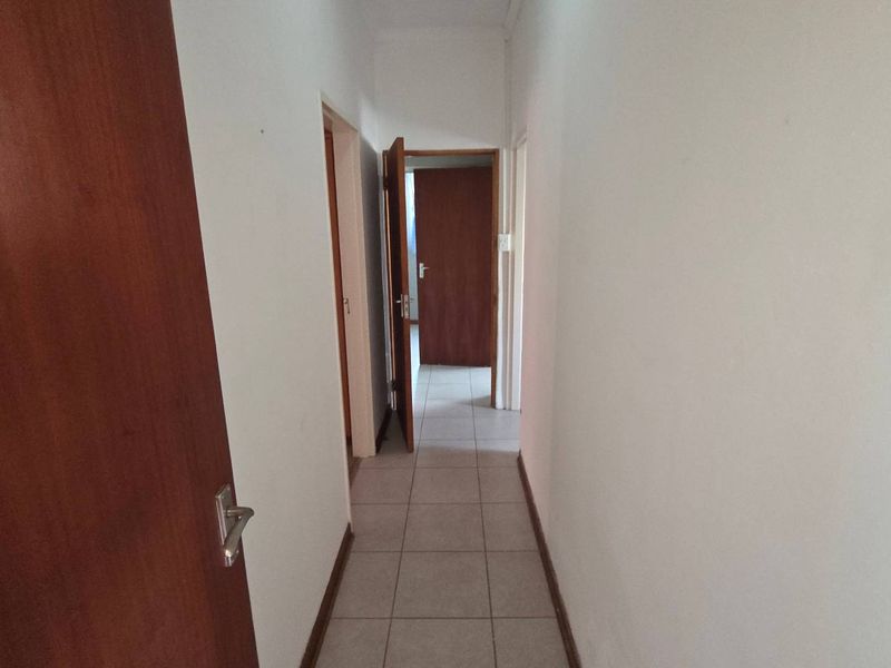 A functional, empty hallway featuring tiled flooring and multiple wooden doors providing access to various rooms within the apartment.