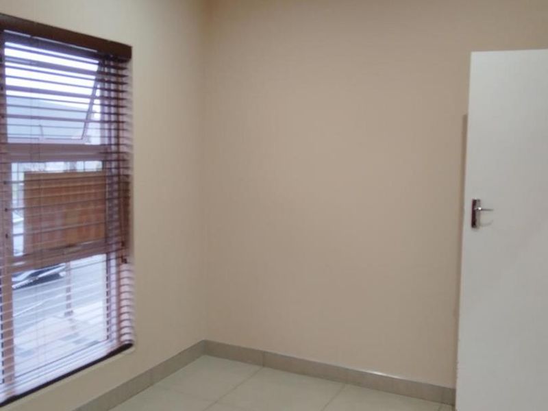A clean, empty office space featuring neutral wall paint, tiled flooring, and a window fitted with venetian blinds.