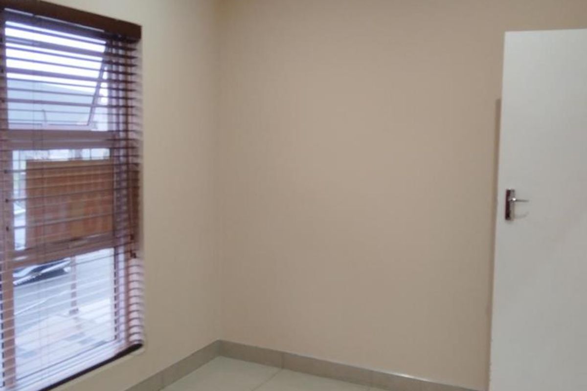 A clean, empty office space featuring neutral wall paint, tiled flooring, and a window fitted with venetian blinds.