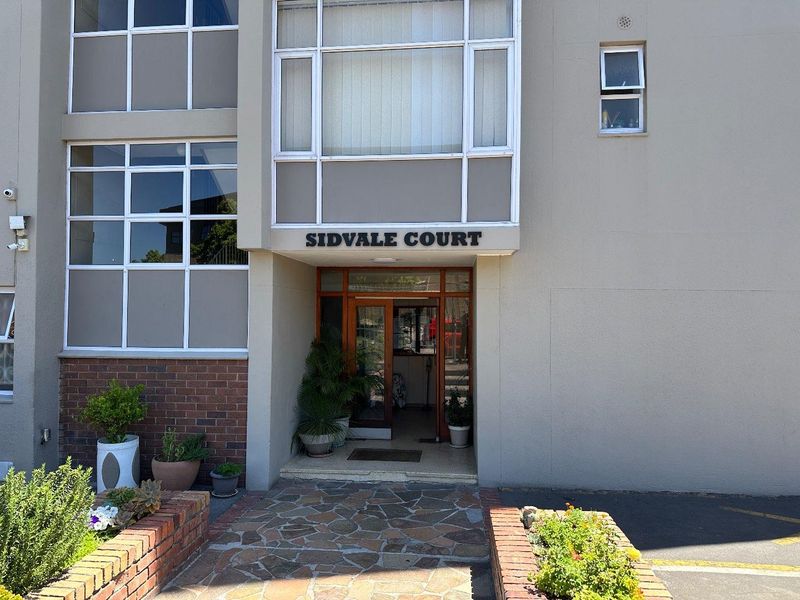 The front entrance of Sidvale Court apartment building, featuring a stone paved walkway, brick planter boxes, and a glass panelled entrance door.