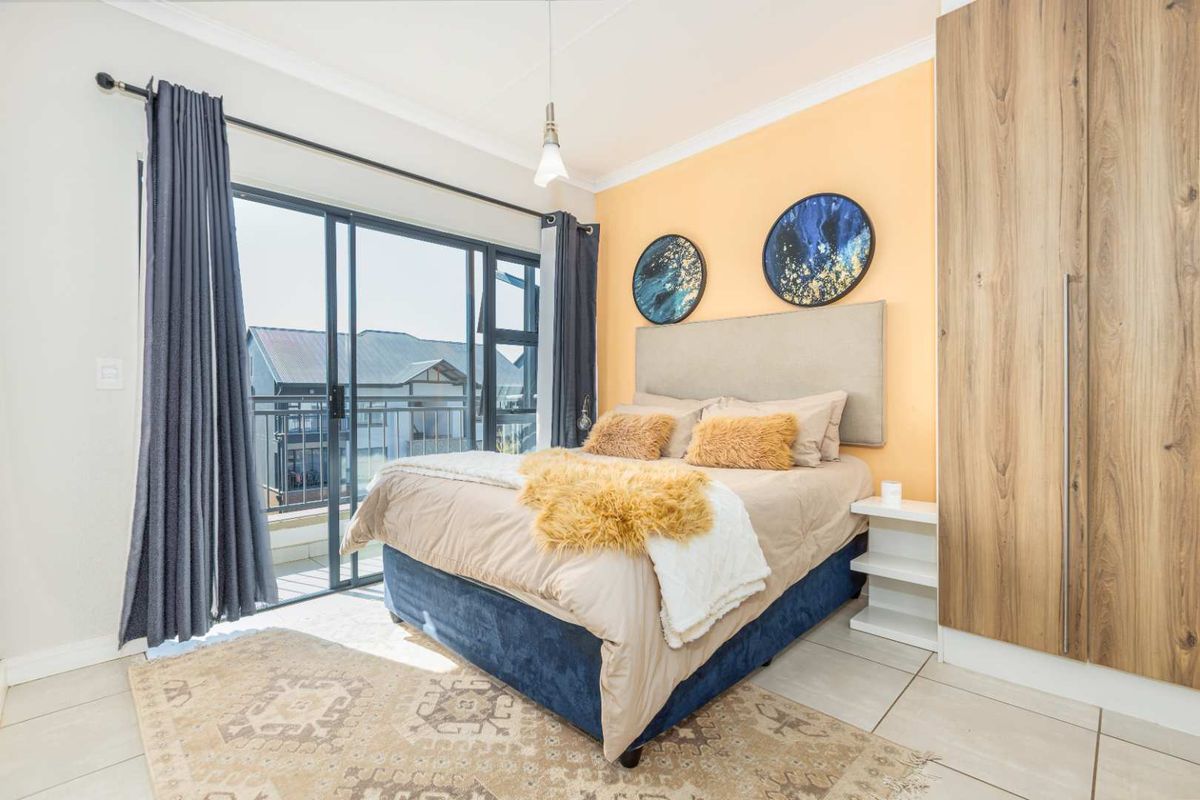 A bright bedroom featuring built-in wooden wardrobes, tiled flooring, and large sliding glass doors that open onto a private balcony.
