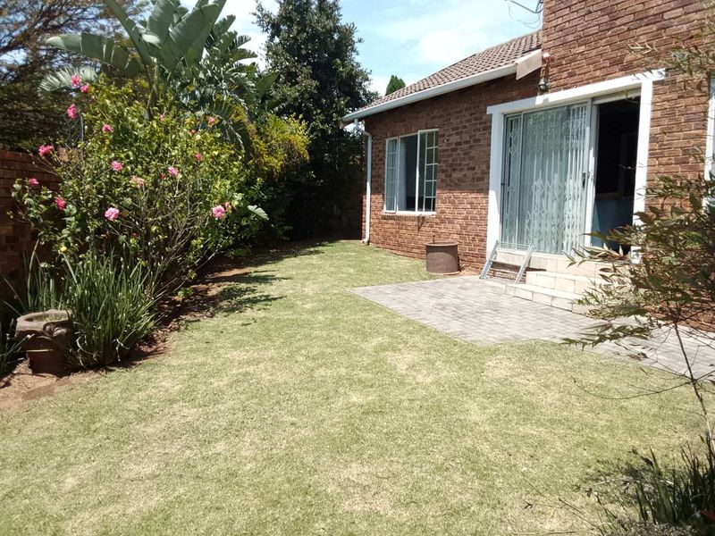 Rear view of the townhouse featuring a brick facade, a paved patio area, and a small private garden with established landscaping.