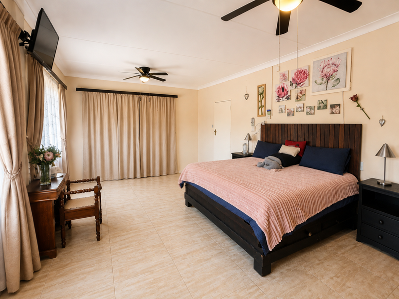 Spacious bedroom featuring neutral tiled flooring, dual ceiling fans, and large windows with floor-to-ceiling curtains, providing a bright and comfortable living space.