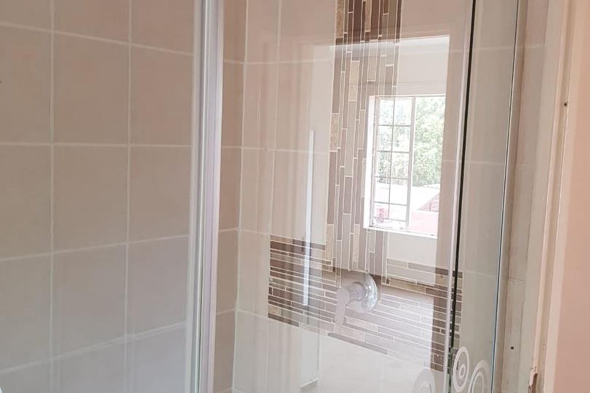 A modern bathroom featuring a glass-enclosed shower with a rainfall showerhead and decorative tiled accent wall.