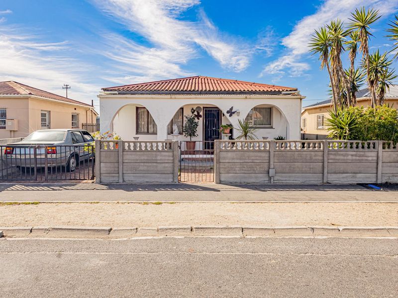 Front elevation of a single-story house featuring an arched veranda, tiled roof, and a secure precast concrete boundary wall with a metal gate.