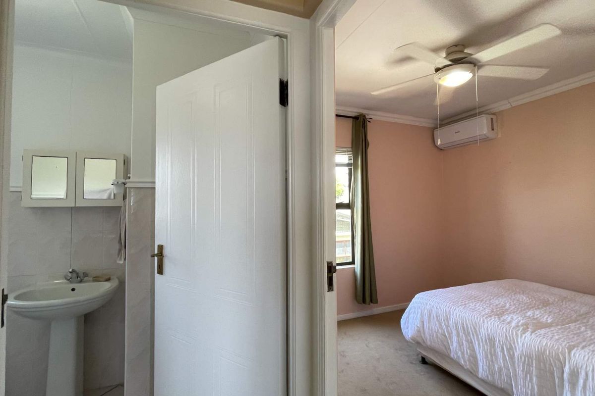 A bedroom featuring a ceiling fan and split-system air conditioner, with an adjacent bathroom area visible through the doorway.