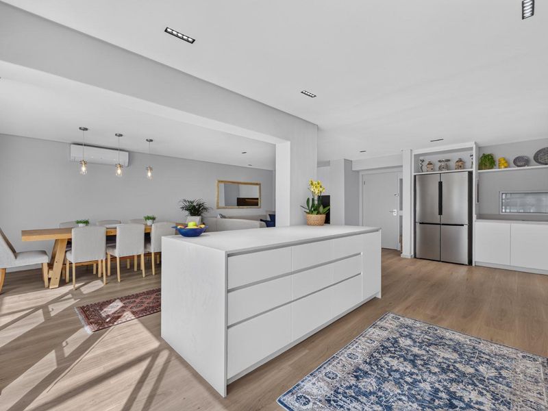Spacious open-plan living and dining area featuring a modern kitchen island, sleek cabinetry, recessed lighting, and light wood-look flooring throughout.