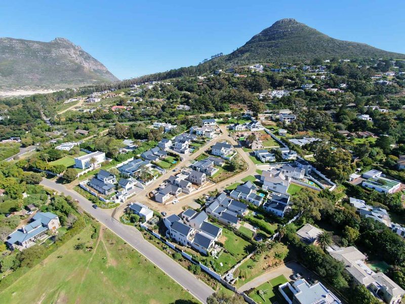 An aerial view of a residential estate development nestled in a scenic valley with mountain views and established landscaping.