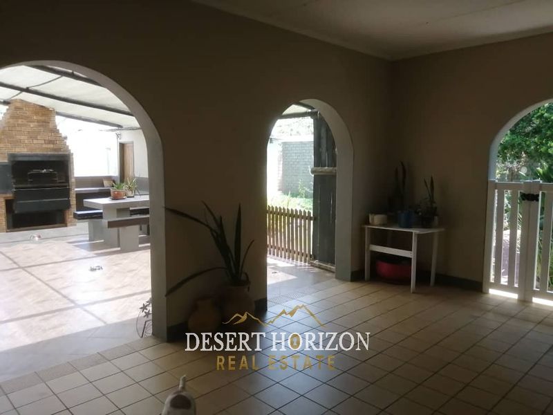 Covered patio area featuring arched architectural details, tiled flooring, and a built-in braai, providing a functional outdoor entertainment space.