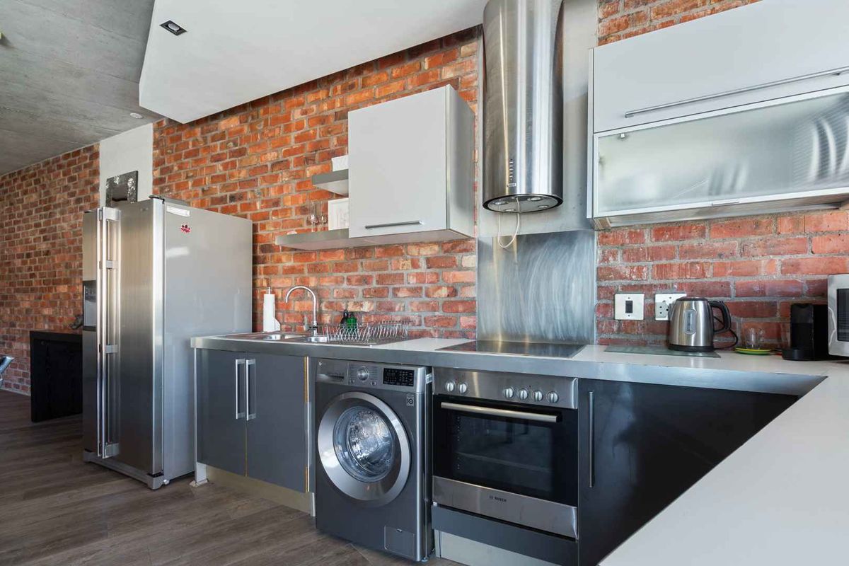 Modern industrial-style kitchen featuring exposed brick walls, stainless steel countertops, integrated cabinetry, and high-quality built-in appliances.