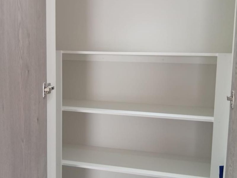 A clean, modern built-in pantry or storage cupboard featuring white shelving and light wood-grain cabinet doors.