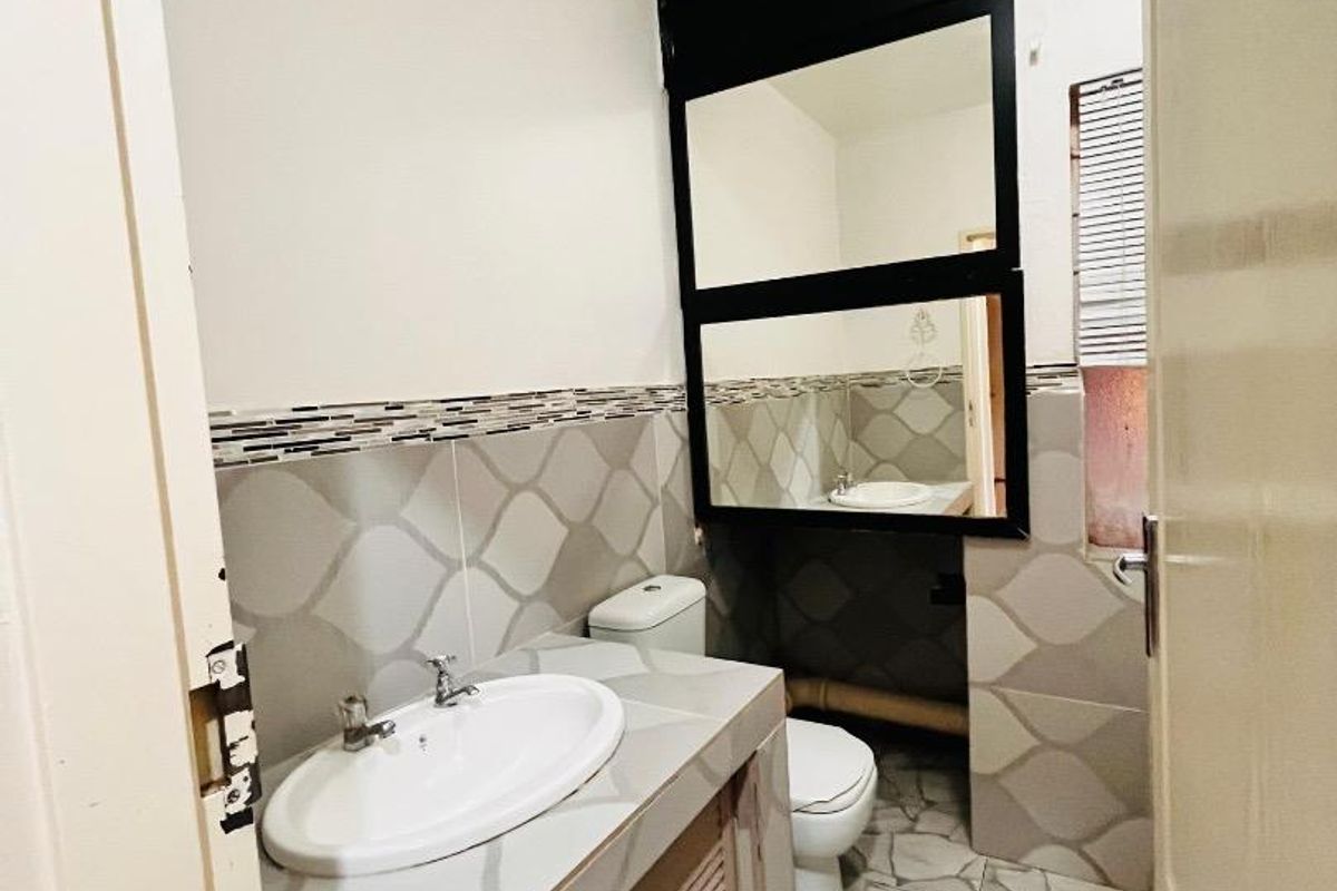 A compact bathroom featuring a built-in vanity with a ceramic basin, a toilet, and decorative wall tiling with a large framed mirror.