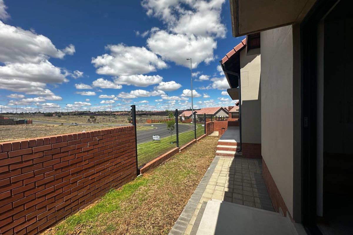 A view of the side exterior area featuring paved pathways, a brick boundary wall, and metal fencing overlooking the surrounding estate landscape.