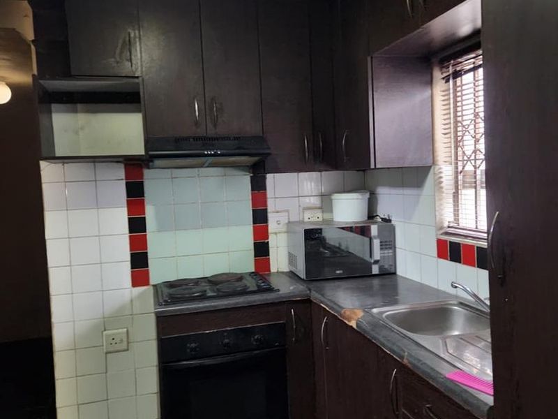 A dated kitchen featuring dark cabinetry, electric cooking appliances, and a stainless steel sink, currently requiring significant ceiling repairs and cosmetic updates.