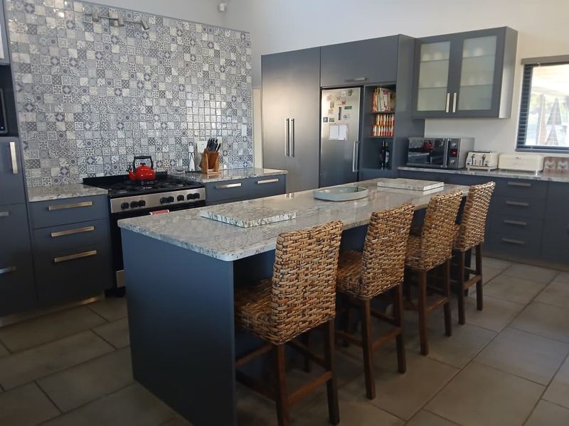 Modern kitchen featuring a large central island with stone countertops, dark cabinetry, a gas stove, and a decorative tiled backsplash.
