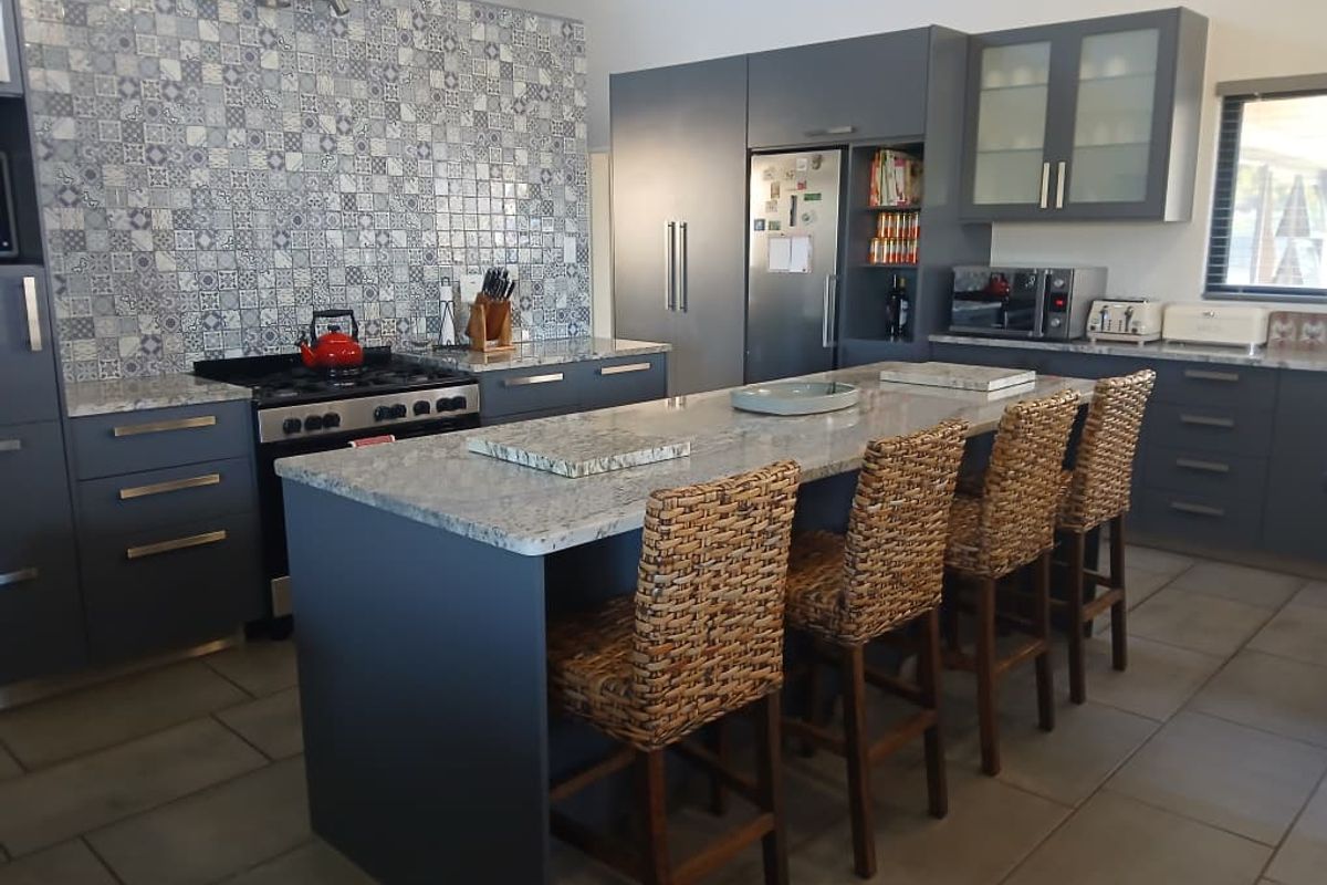 Modern kitchen featuring a large central island with stone countertops, dark cabinetry, a gas stove, and a decorative tiled backsplash.