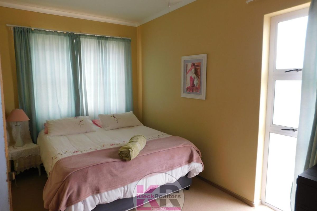 A standard bedroom featuring neutral wall tones, carpeted flooring, and a large window providing natural light.