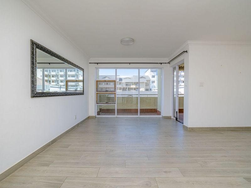 A bright, empty living room featuring modern laminate flooring, coved cornicing, and large sliding glass doors leading to an outdoor balcony area.