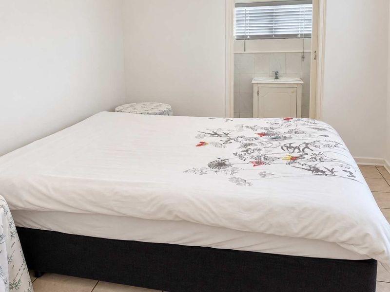 A bedroom featuring tiled flooring and an adjoining en-suite bathroom area with a built-in vanity and window blinds.