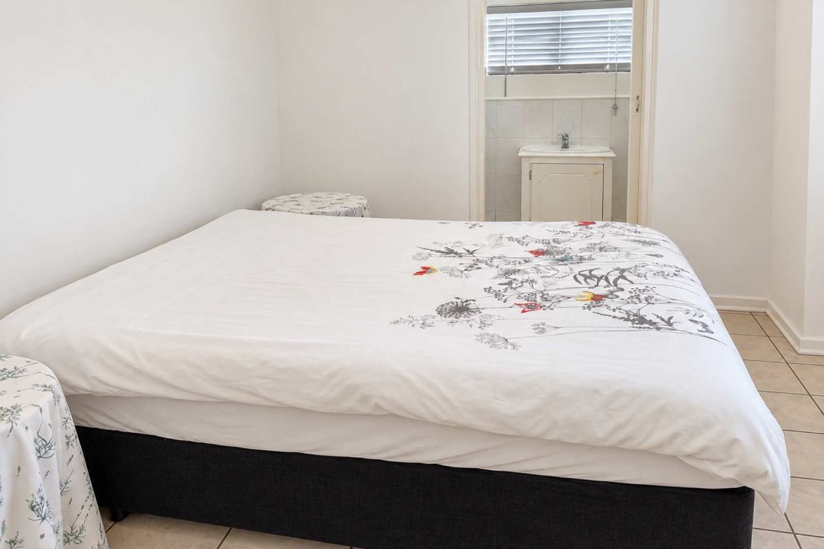 A bedroom featuring tiled flooring and an adjoining en-suite bathroom area with a built-in vanity and window blinds.