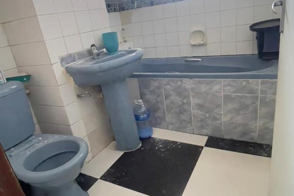 A dated bathroom featuring a blue pedestal sink, matching toilet, and bathtub with a checkerboard tile floor and wall-mounted water heater.
