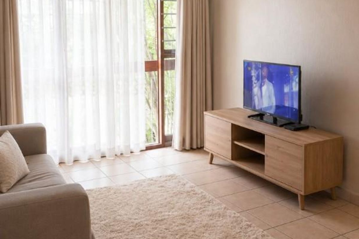 A neutrally decorated living room featuring tiled flooring and a large sliding glass door providing natural light and access to the exterior.
