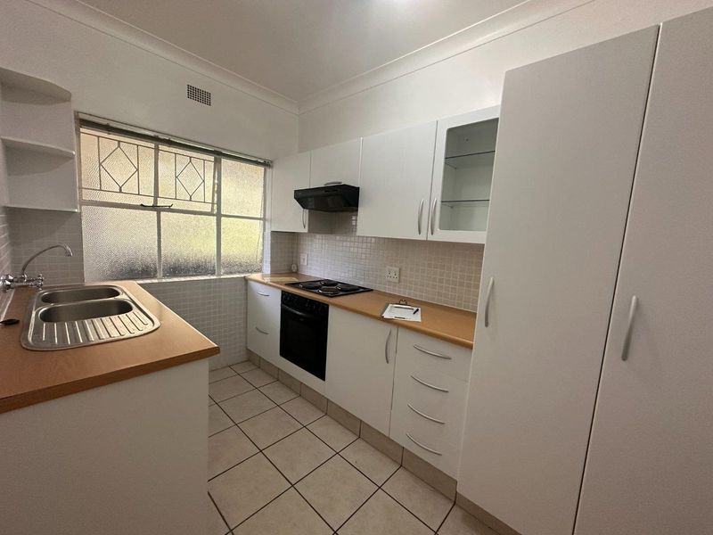 A clean and functional kitchen featuring white cabinetry, laminate countertops, built-in oven, electric hob, and tiled flooring.