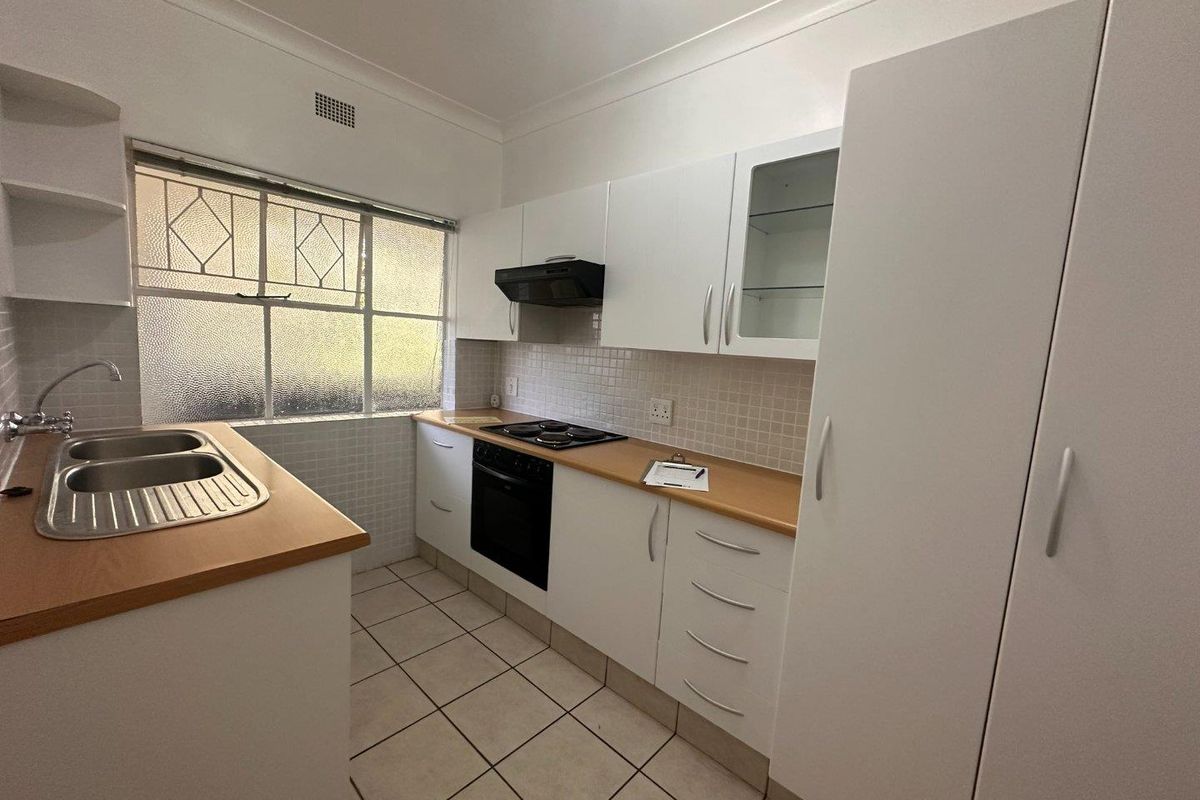 A clean and functional kitchen featuring white cabinetry, laminate countertops, built-in oven, electric hob, and tiled flooring.