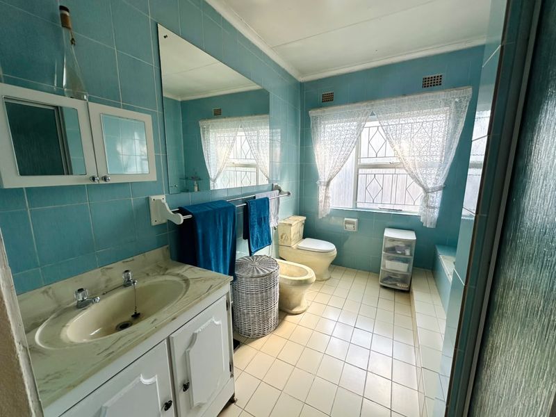 A dated bathroom featuring blue wall tiles, a vanity with integrated basin, toilet, bidet, and a built-in bathtub.