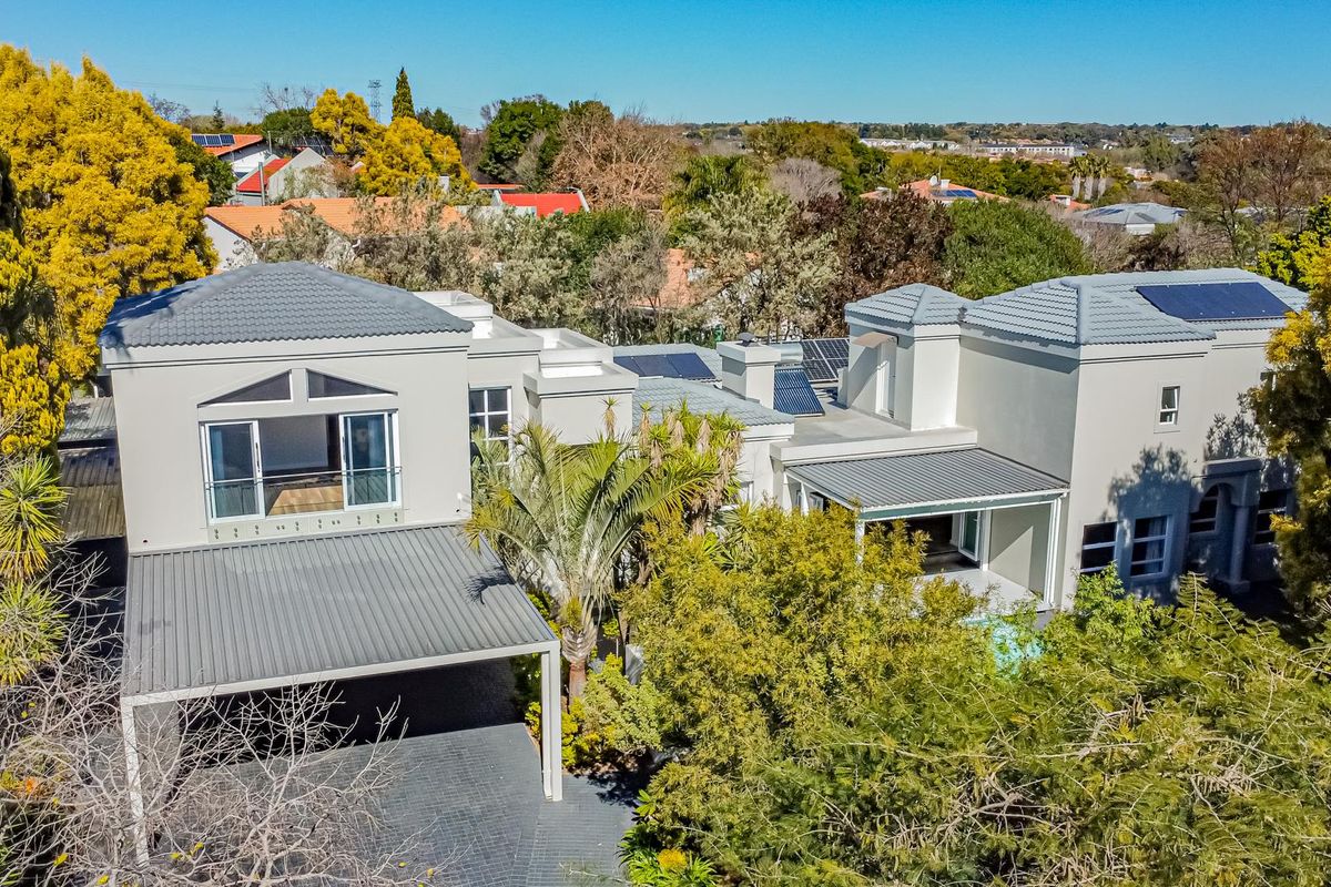 Aerial view of a modern multi-level residential property featuring a tiled roof, solar panels, paved driveway, and covered outdoor patio areas.