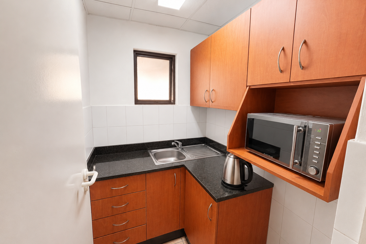 A compact office kitchenette featuring wood-finish cabinetry, a dark stone countertop, a stainless steel sink, and a built-in microwave shelf.