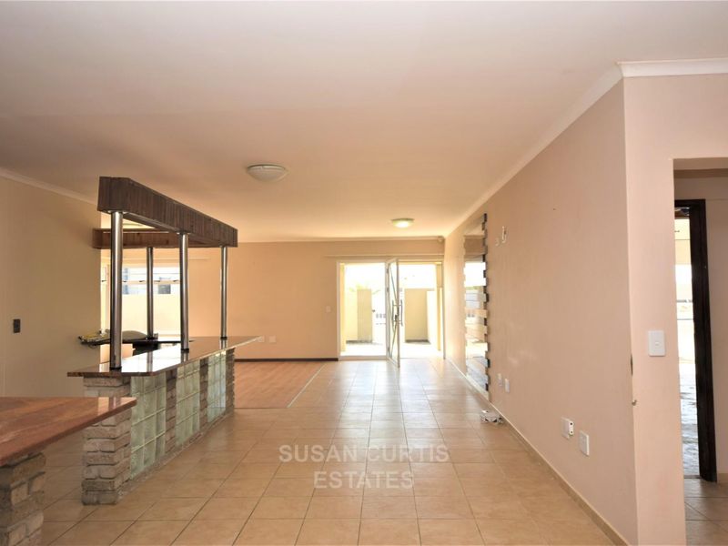 Spacious open-plan living area featuring a built-in bar with glass block detailing and tiled flooring, leading out to an exterior patio area.