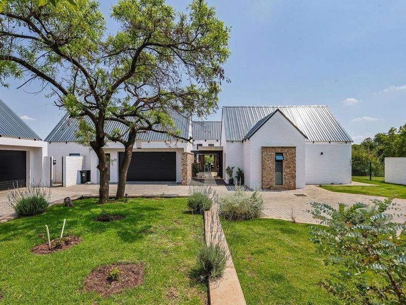 A modern farmhouse-style home featuring a white brick facade, stone accents, metal roofing, and a well-maintained front garden with a paved driveway.