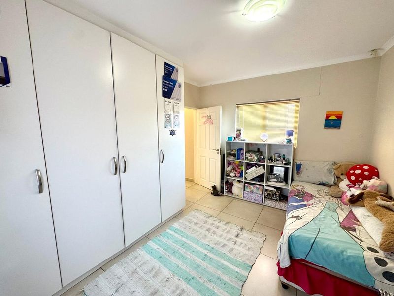 A functional bedroom featuring built-in cupboards, tiled flooring, and natural light through a window with venetian blinds.