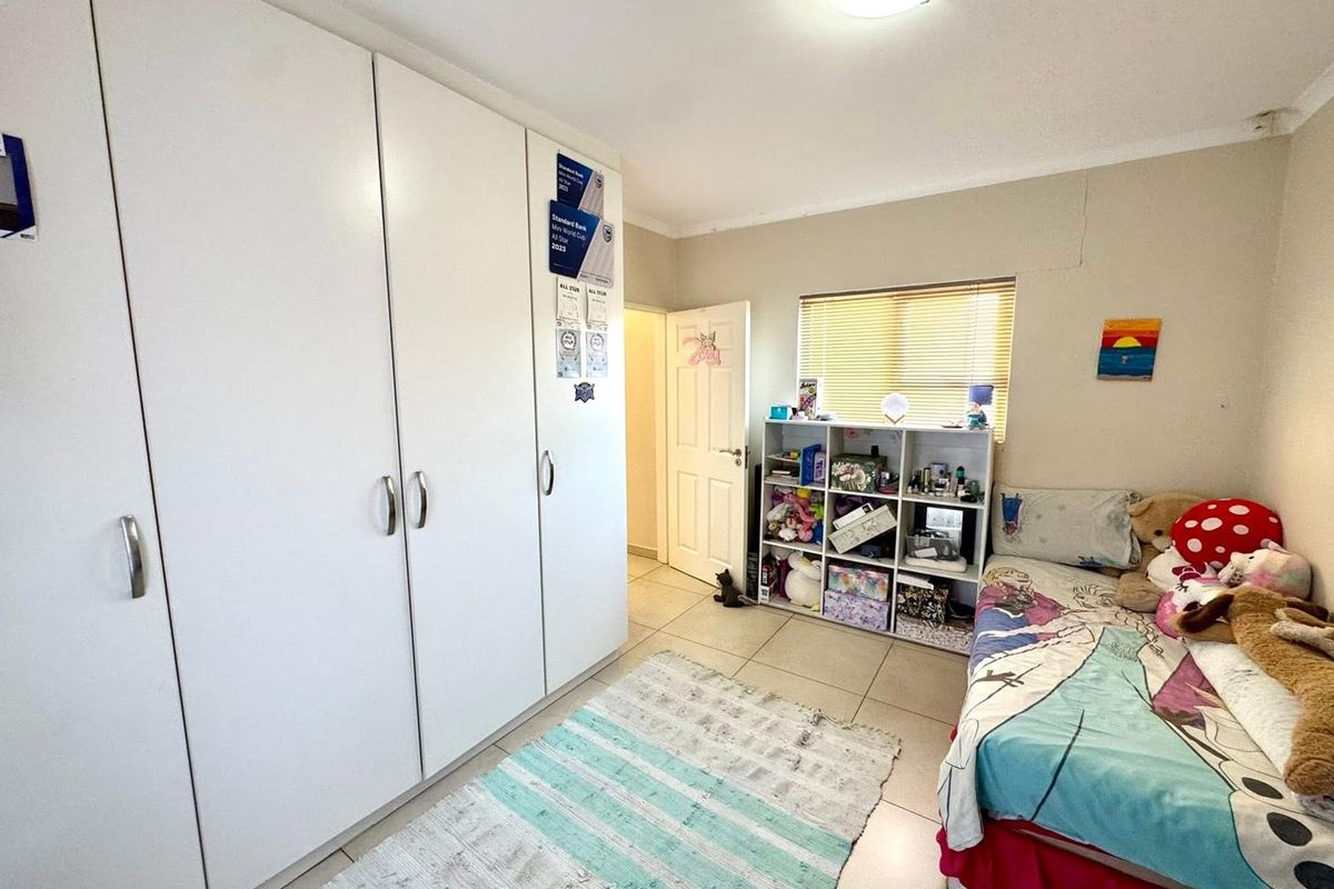 A functional bedroom featuring built-in cupboards, tiled flooring, and natural light through a window with venetian blinds.