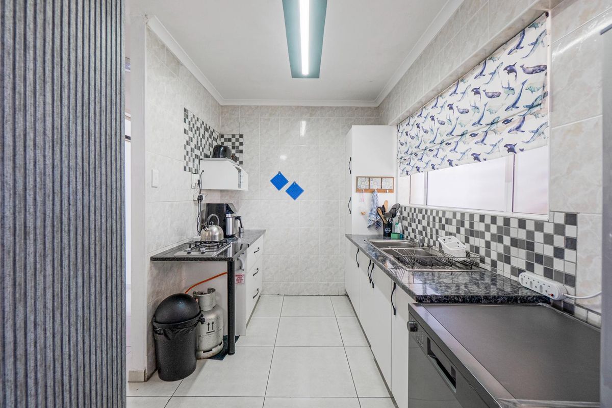 A functional galley-style kitchen featuring granite countertops, tiled walls, double stainless steel sink, and built-in cabinetry.