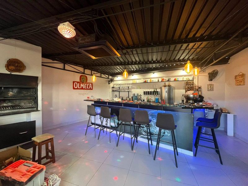 A dedicated entertainment bar area featuring a built-in bar counter, integrated shelving, and a built-in braai under an exposed metal ceiling.
