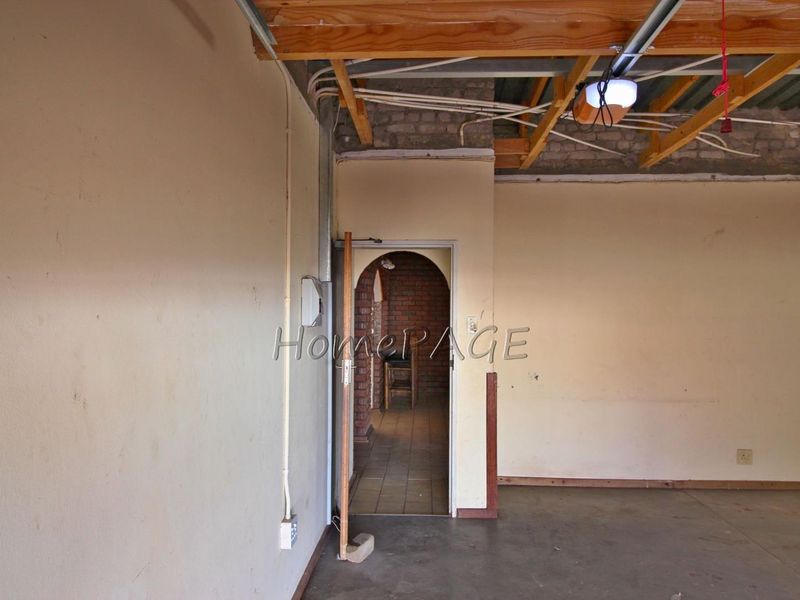 An unfinished garage space featuring exposed timber roof trusses, exposed brickwork, and an arched doorway leading to an adjacent room.