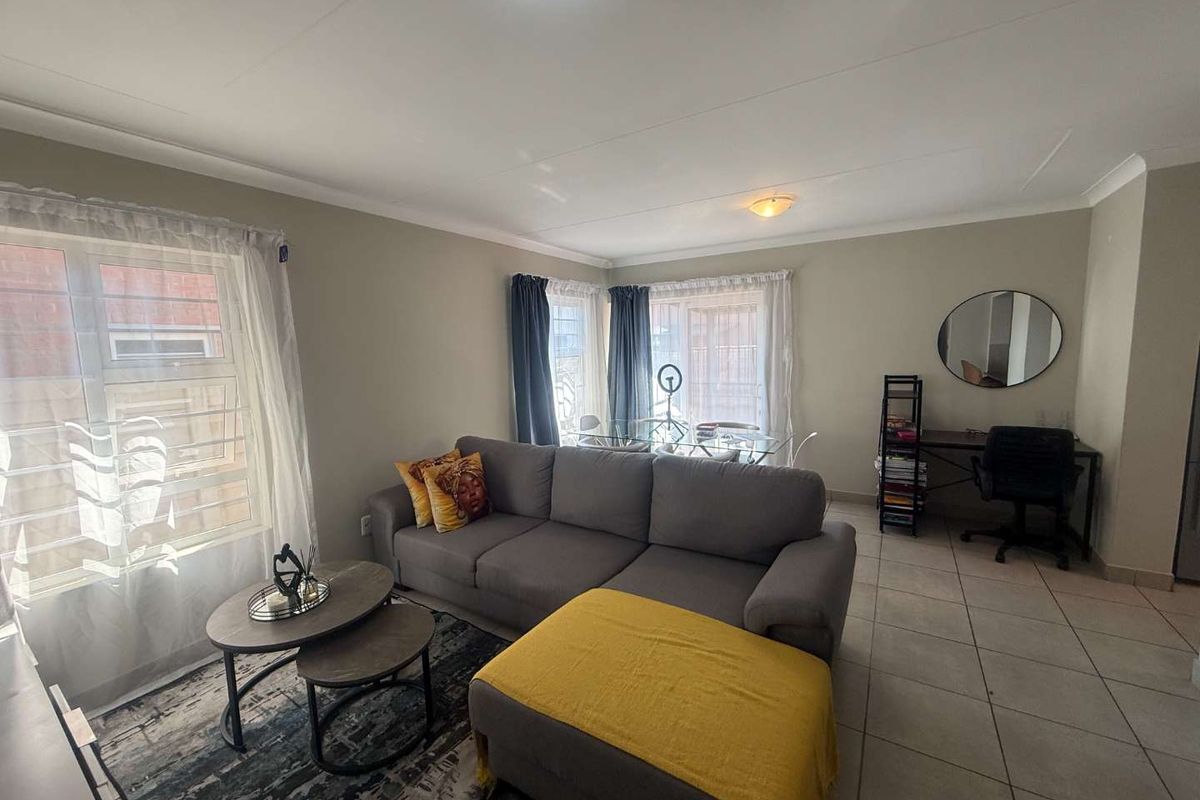 A bright and functional living area featuring tiled flooring, neutral wall tones, and large windows with security bars, offering a comfortable and versatile living space.